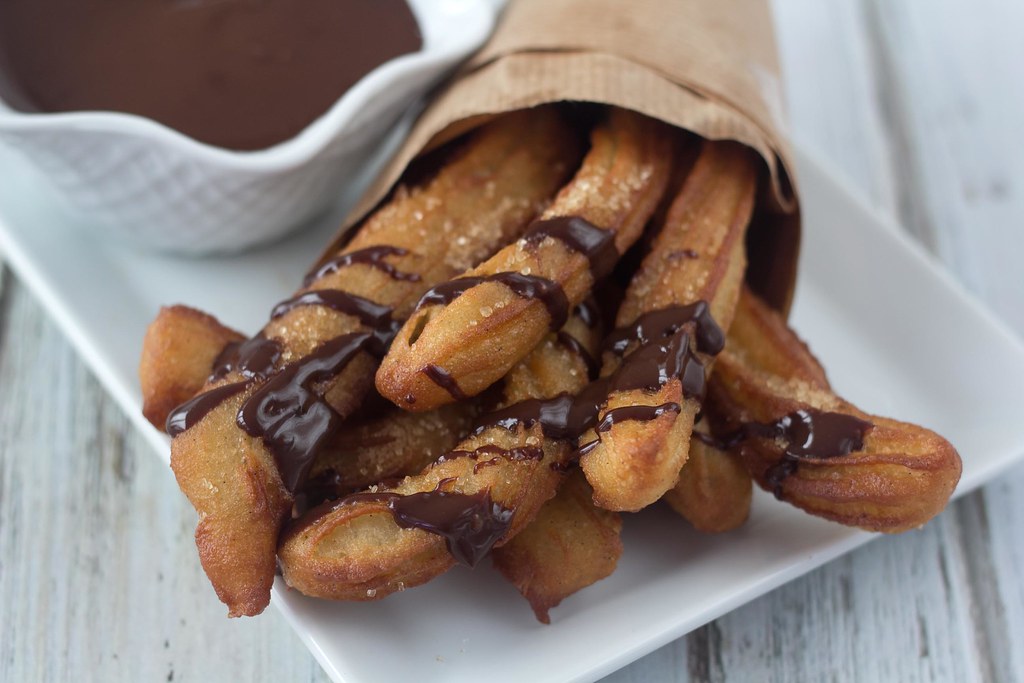 Churros eller spanskrør serveret med chokoladesovs på et fad og i kræmmerhus