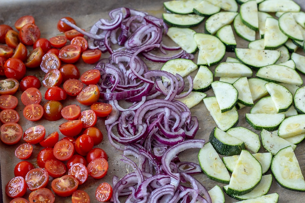 Tomater, rødløg og squash på en bageplade før ovnen